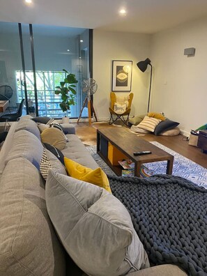 Relax in this stylish living room with a large sofa, coffee table, and floor lamp, opening to a serene outdoor space.