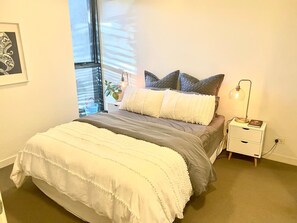 Relax in a serene bedroom with a large bed, bedside table, and reading lamp, accompanied by a personal touch from a framed artwork.