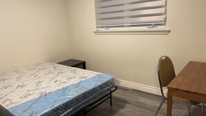 A small, sparsely furnished room with a bed, a small table, and a chair.