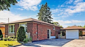 A single-story brick house with a garage, a front yard, and a large tree in the background.