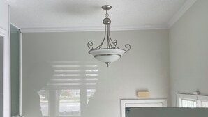 A room with a chandelier, a window with blinds, and a door.