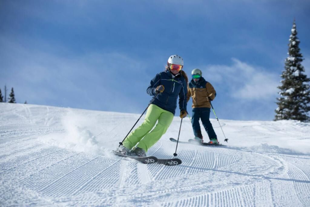 Two skiers on a snowy slope with a clear sky.