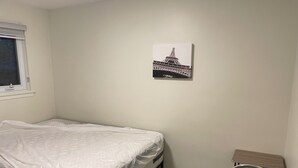 Une chambre avec un lit simple, un petit bureau, une chaise et une image de la Tour Eiffel accrochée au mur.