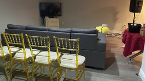 Un salon avec un canapé gris, des fauteuils jaunes, un téléviseur et un haut-parleur posé sur une table.
