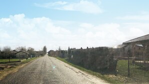 Une route de campagne bordée de bâtiments des deux côtés, notamment une grange et un espace clôturé.