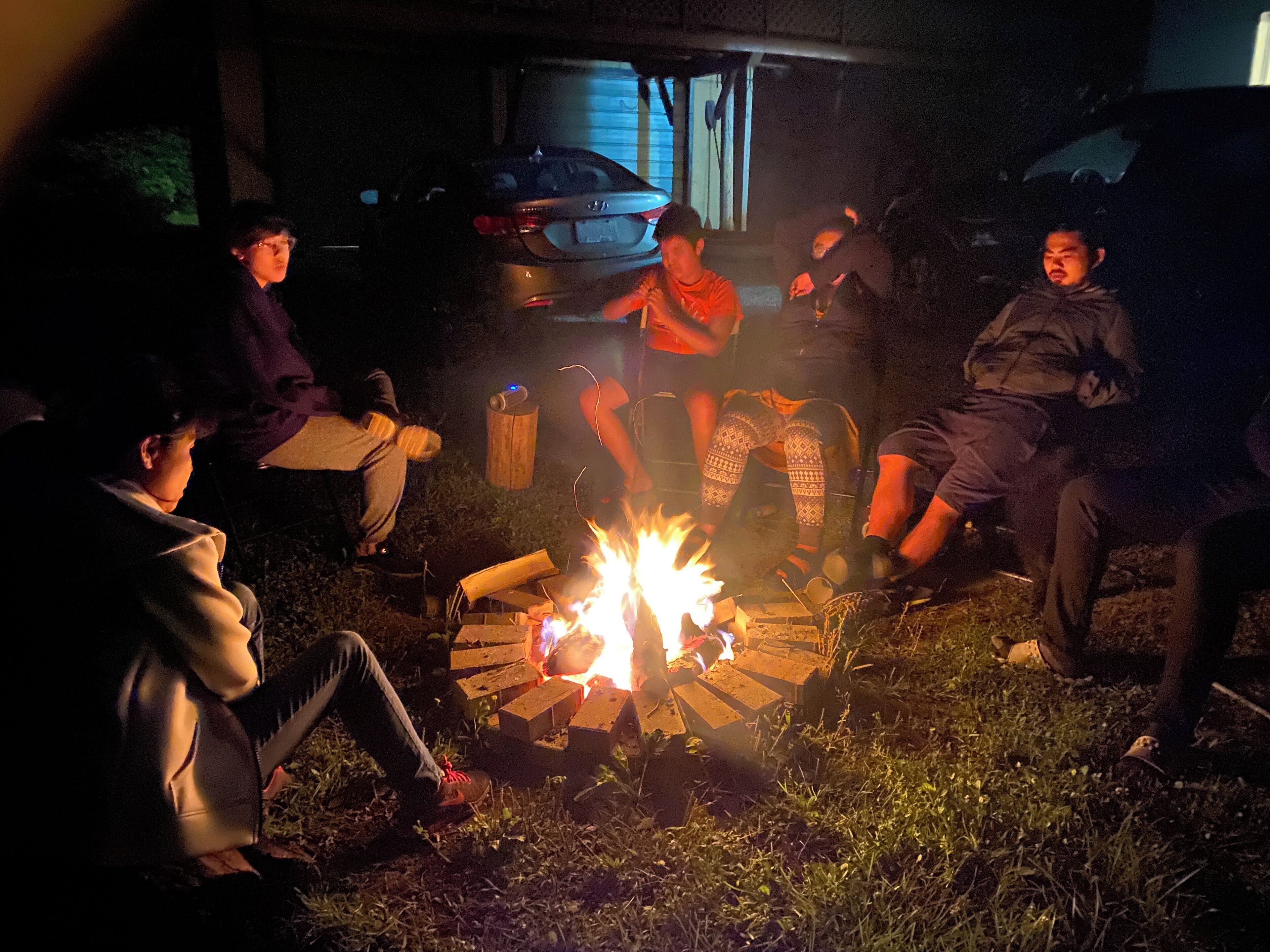 A group of people sitting around a campfire outdoors at night.