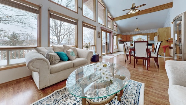 A spacious living room with a large glass coffee table, a beige sofa with decorative pillows, and a dining area with wooden chairs and a red accent chair. - Charming lakefront cottage on Little Doe Lake in Muskoka area (Katrine)