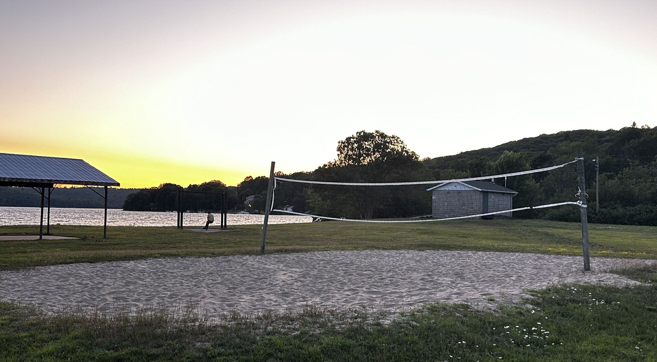 A volleyball court with a net, a covered pavilion, and a small shed.