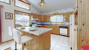 A kitchen with wooden cabinets, a granite countertop, a white dining area, and a view through the window. - Charming lakefront cottage on Little Doe Lake in Muskoka area (Katrine)