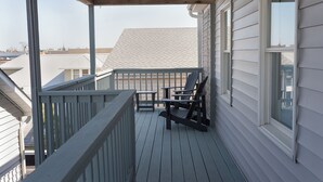 A covered porch with a wooden railing, a table, and two Adirondack chairs.