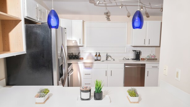 A modern kitchen with white cabinets, a black refrigerator, and two blue pendant lights.