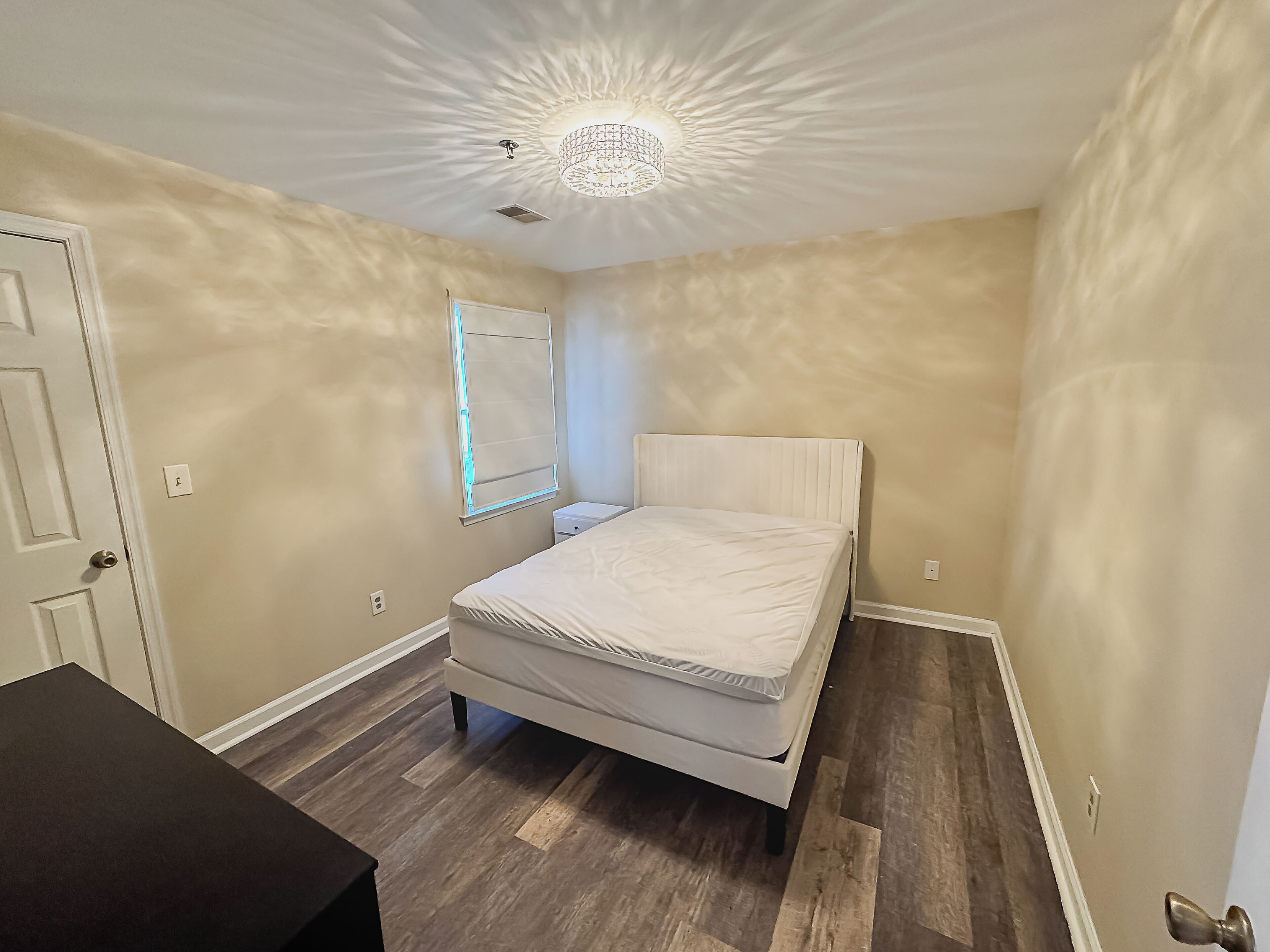 A bedroom with a bed, a nightstand, a dresser, and a ceiling light fixture.
