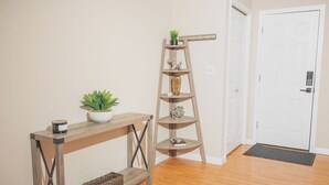 A wooden console table with a potted plant and a candle, a wooden ladder shelf with decorative items, and a door with a doormat.
