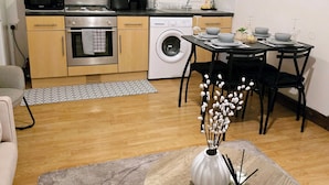 A compact kitchen with a microwave, oven, and washing machine. There is a dining table with chairs and a vase with flowers. - Southampton City View Apartment (Southampton)
