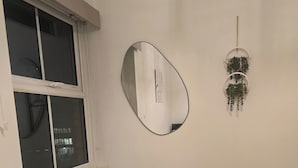 A bedroom with a bed, a window, a wall-mounted mirror, and a hanging plant. - Southampton City View Apartment (Southampton)