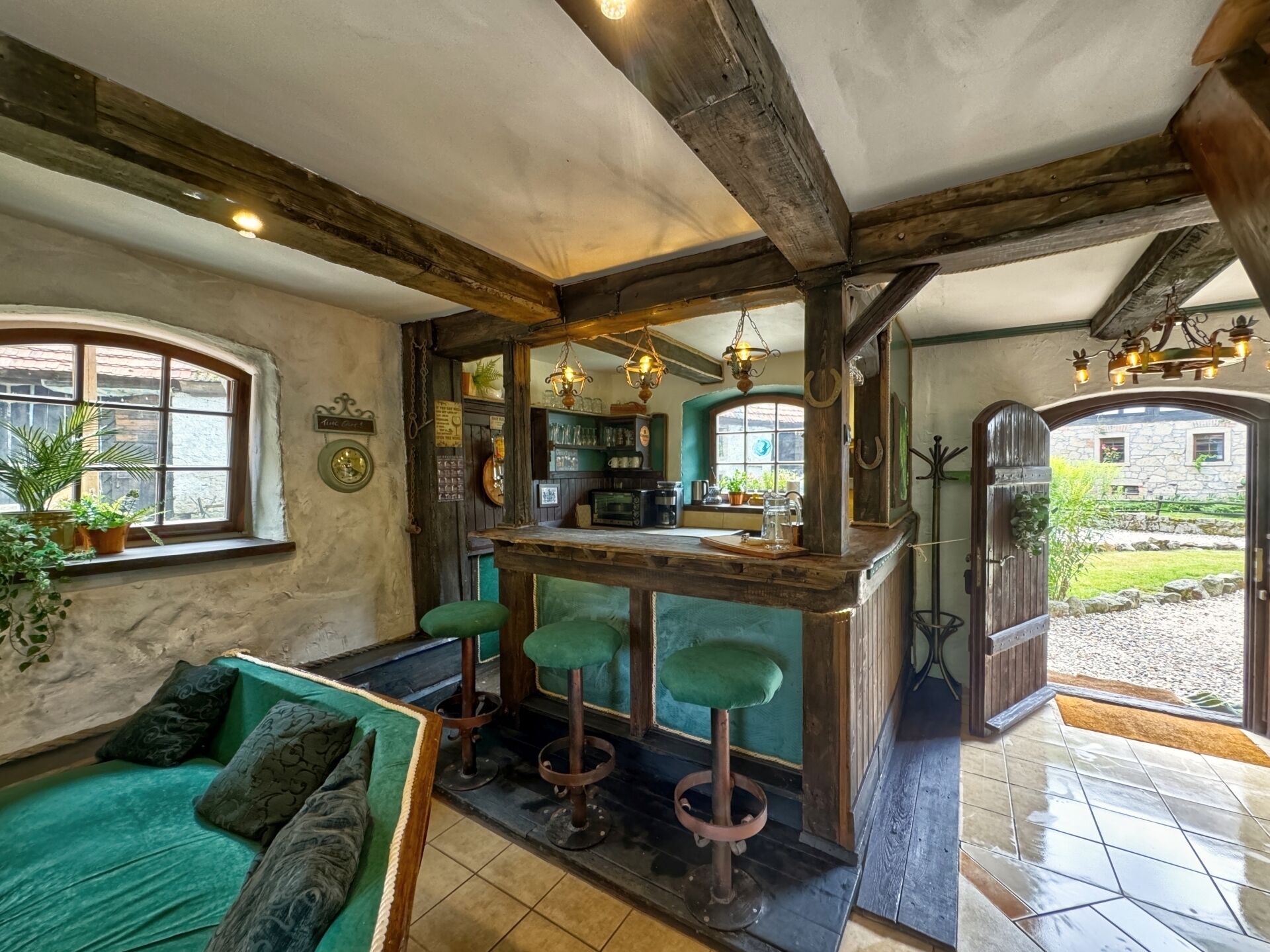 Un interior rústico con una zona de bar, asientos verdes y vistas al jardín.