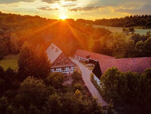 Ett hus på landsbygden med ett sluttande tak, omgivet av täta träd och en klar himmel.