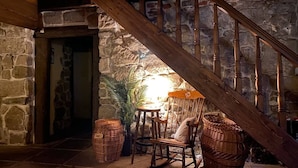 A rustic interior with a stone wall, wooden staircase, wicker furniture, and a table with a lamp. - The Oak Lodge (Lwowek Slaski)
