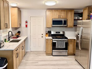 Una cucina con mobili in legno, un frigorifero in acciaio inossidabile, un forno a microonde, un fornello e un lavello.
