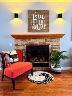 Un salon avec une cheminée, un canapé rouge, un coussin décoratif, un panneau mural et une plante en pot.