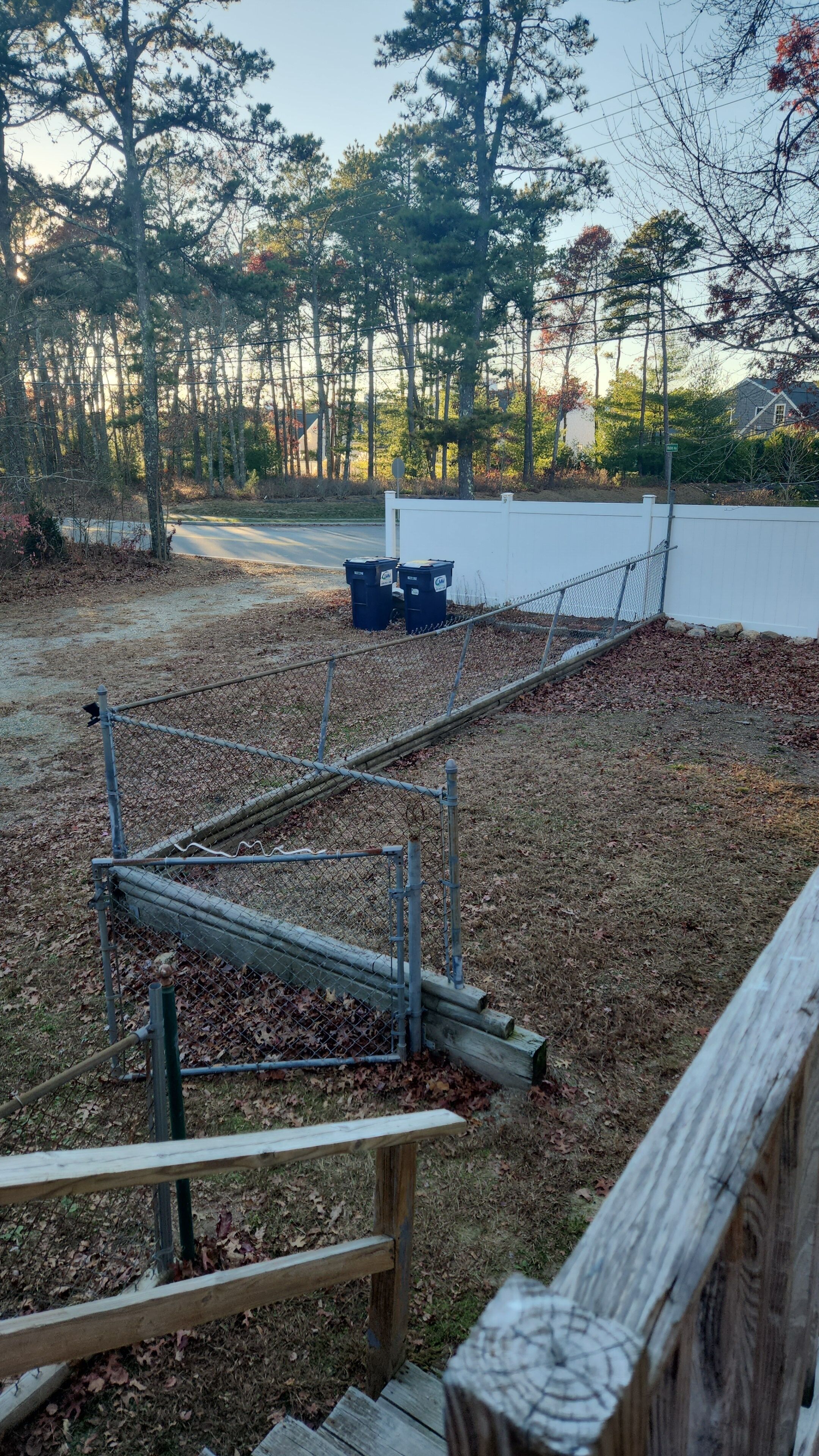 A fenced outdoor area with a wooden bench, a chain-link fence, and a white wall in the background.