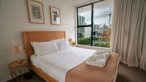 A neatly made bed with white linens, a wooden headboard, and a view of buildings through a large window. - Eclectic City-Fringe Townhouse with Rooftop Deck (Auckland)