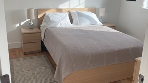 A bedroom with a wooden bed, two bedside tables, a rug, and a framed picture on the wall. - Convenient and bright Cross Trail Vacation Getaway! (Sitka)