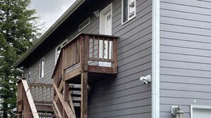 A two-story house with a wooden staircase leading to a balcony. - Convenient and bright Cross Trail Vacation Getaway! (Sitka)