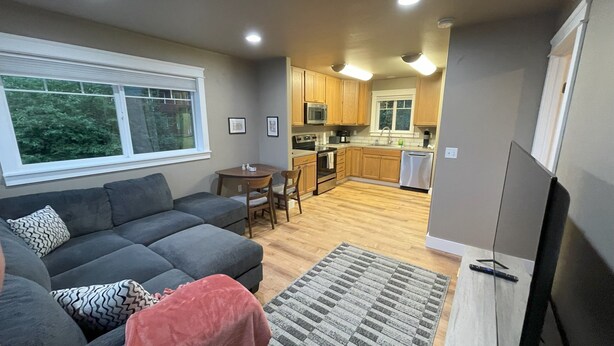 A modern living room with a gray sofa, a small dining table, and a kitchen in the background. - Convenient and bright Cross Trail Vacation Getaway! (Sitka)