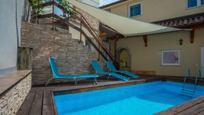 A swimming pool with a stone wall and wooden deck, accompanied by two lounge chairs. - 2 bedroom stunning apartment in Veli Brgud (Veli Brgud)