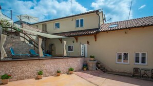 A two-story building with a tiled roof, a stone wall, and a small patio area with blue chairs and potted plants. - 2 bedroom stunning apartment in Veli Brgud (Veli Brgud)