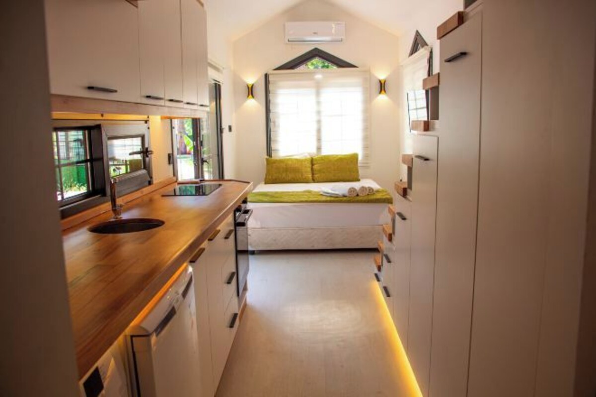 Una cocina compacta con encimera de madera, lavavajillas integrado y ventana con un cojín verde sobre la cama.