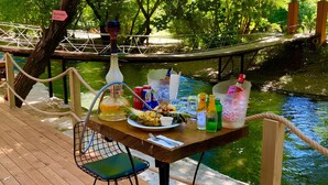Una terraza de madera con una mesa lista para una comida, con vista a un río y rodeada de árboles.
