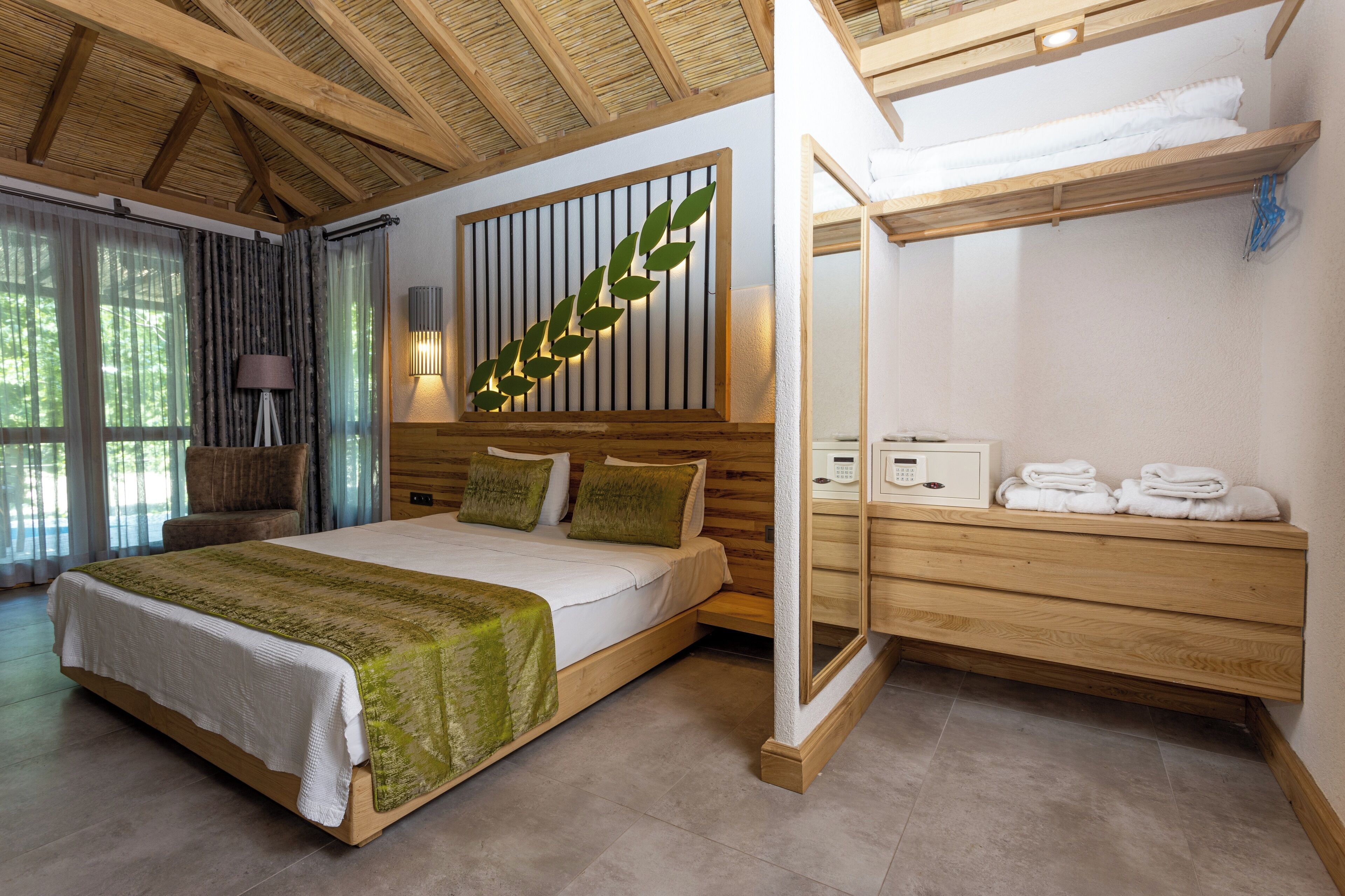 A modern bedroom with a large bed, wooden headboard, a wall-mounted light, and a wooden bench with towels.