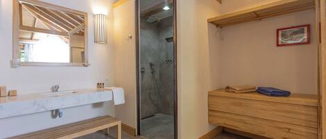 Ein modernes Badezimmer mit Marmorwaschbecken, einer Holzbank, einer Glasdusche und einem Holzwaschtisch mit Handtüchern.