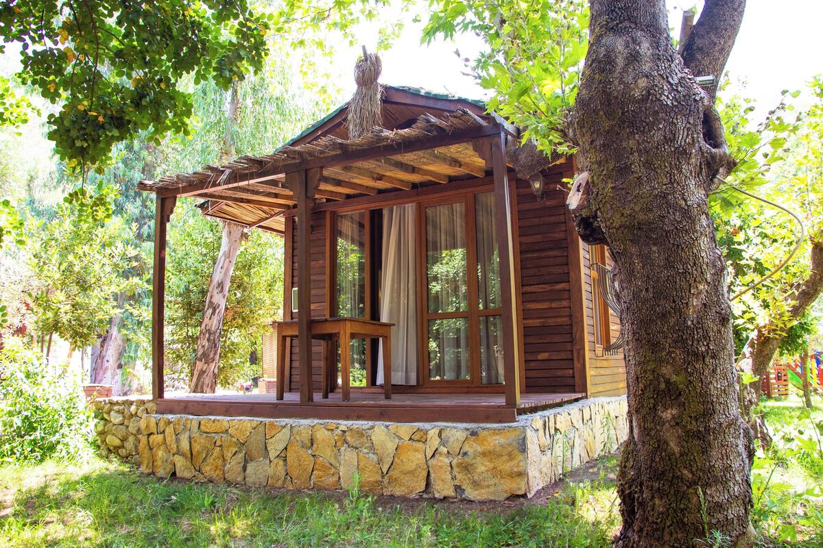 Una cabaña de madera con base de piedra, ventanas amplias y un porche de madera.