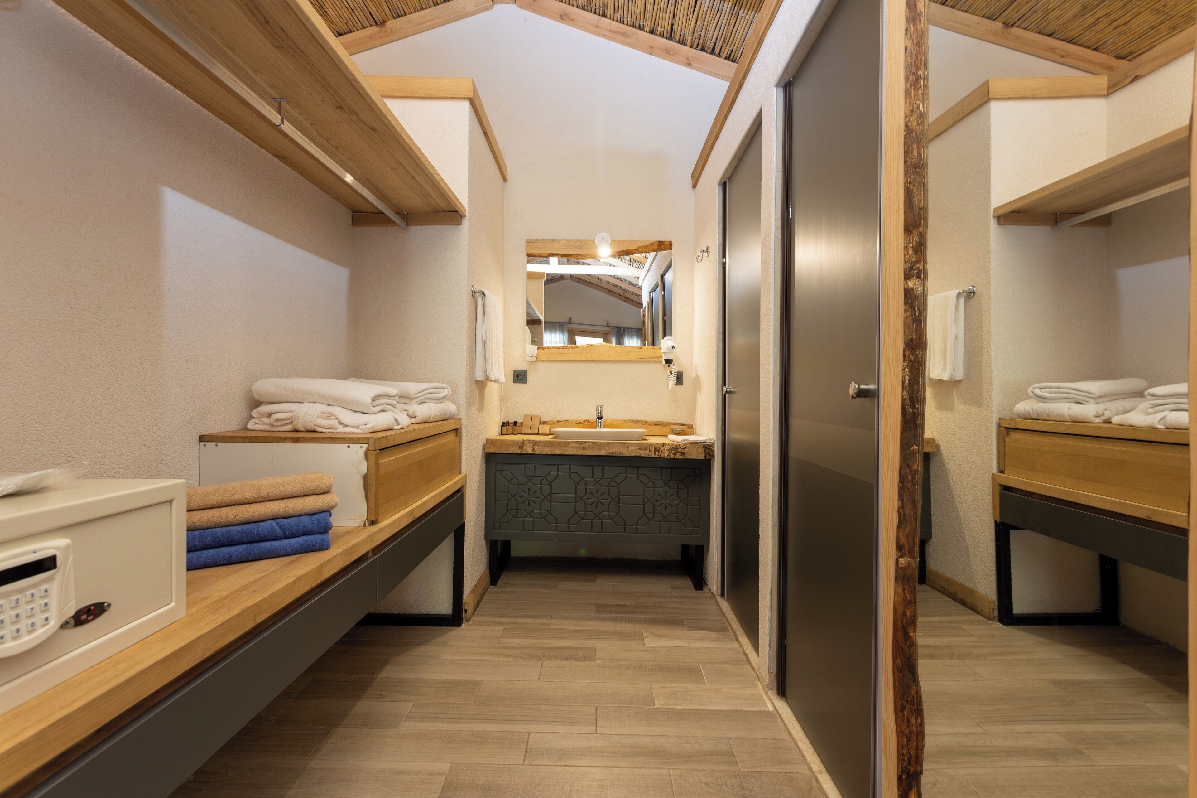 Ein kompaktes, modernes Badezimmer mit Holzboden, einem Waschbecken und einem Spiegel. Auf den Ablagen liegen Handtücher und eine kleine Sitzbank.