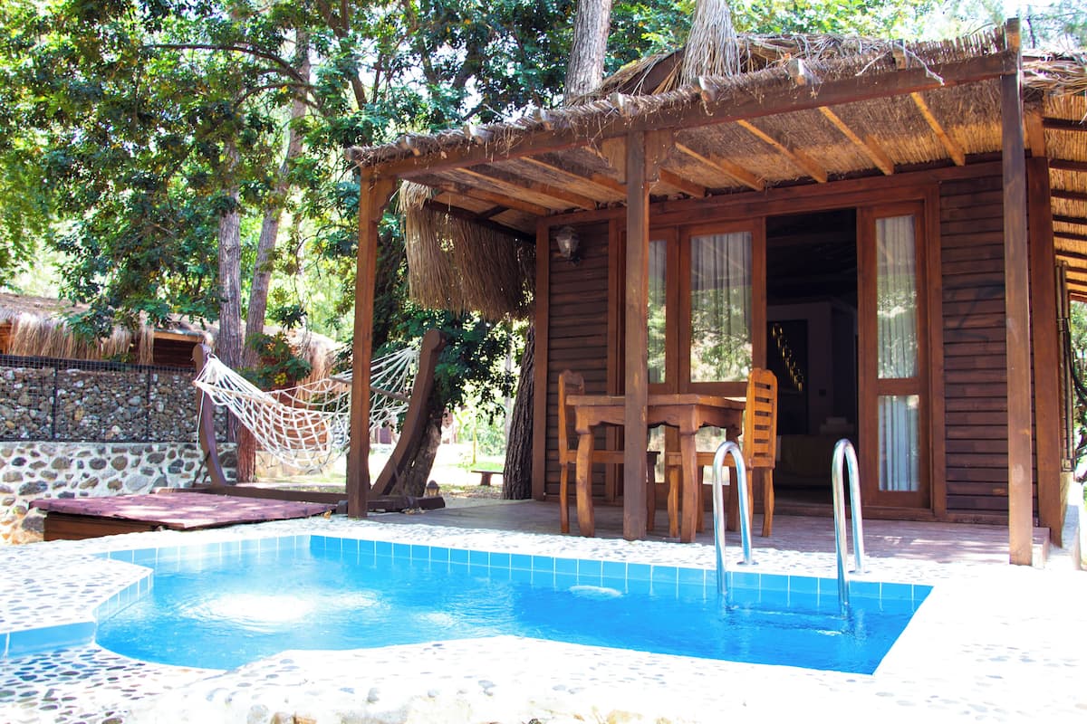 Una cabaña de madera con piscina, rodeada de árboles y un muro de piedra.