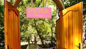 Un arco de madera con un letrero que dice "SUNA" que da a un camino rodeado de árboles.