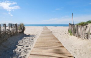 En träpromenad som leder till en sandstrand med en klar himmel.