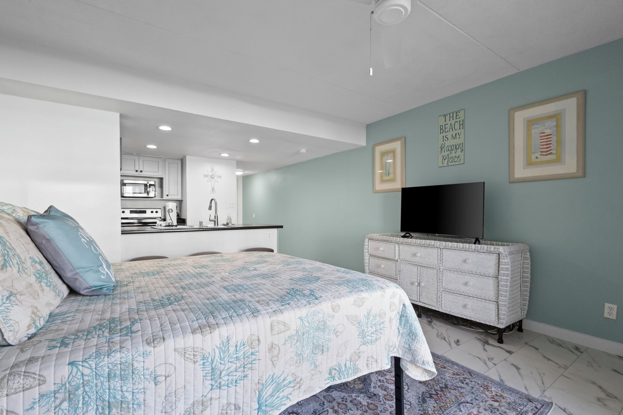 Une chambre à coucher avec un lit, une commode, un téléviseur et, au fond, une cuisine.
