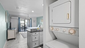 A modern kitchen with a sink, countertop, and a large appliance. There is a window with blue curtains and a door leading to another room.