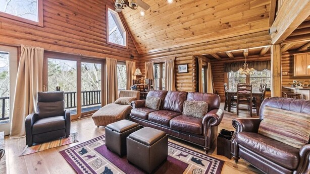 A log cabin interior with a leather sofa, ottomans, and a dining area.