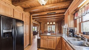 A wooden cabin kitchen with a large refrigerator, wooden cabinets, a granite countertop, and a dining area with a table and chairs.