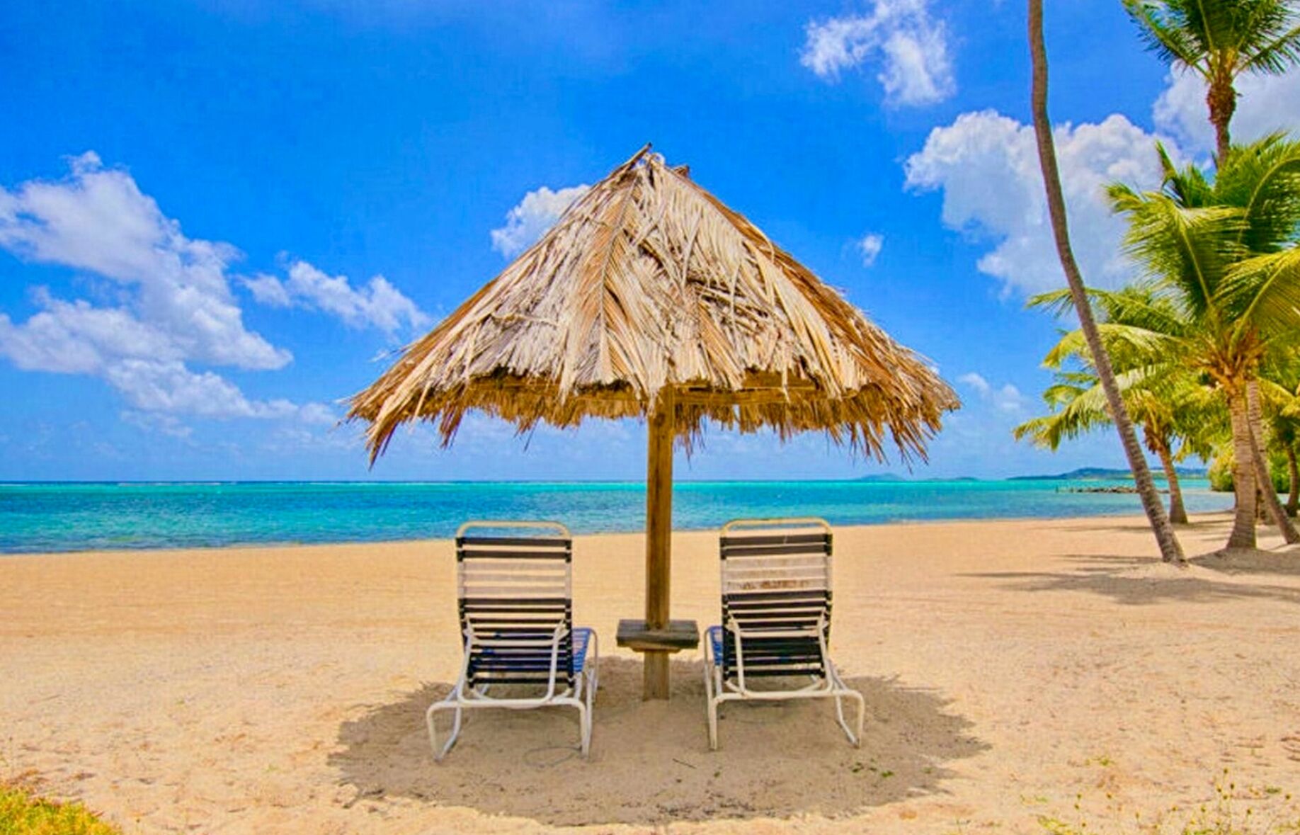 A beach with two lounge chairs and a thatched umbrella.