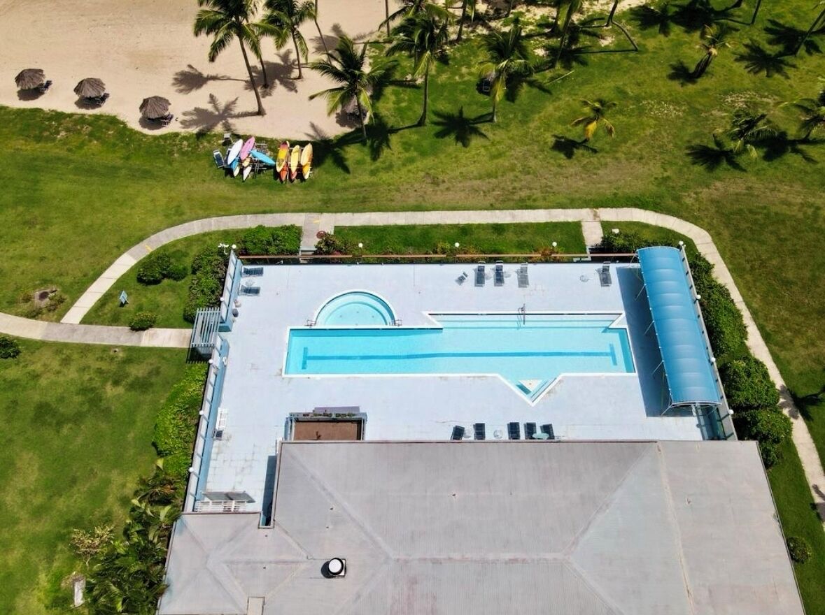 Luftaufnahme eines Resorts mit Schwimmbad, Palmen und Strandstühlen.