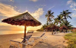 A beach with thatched umbrellas and lounge chairs, palm trees, and a sunset view. - Beachfront Studio Condo @Club St Croix (St Croix)