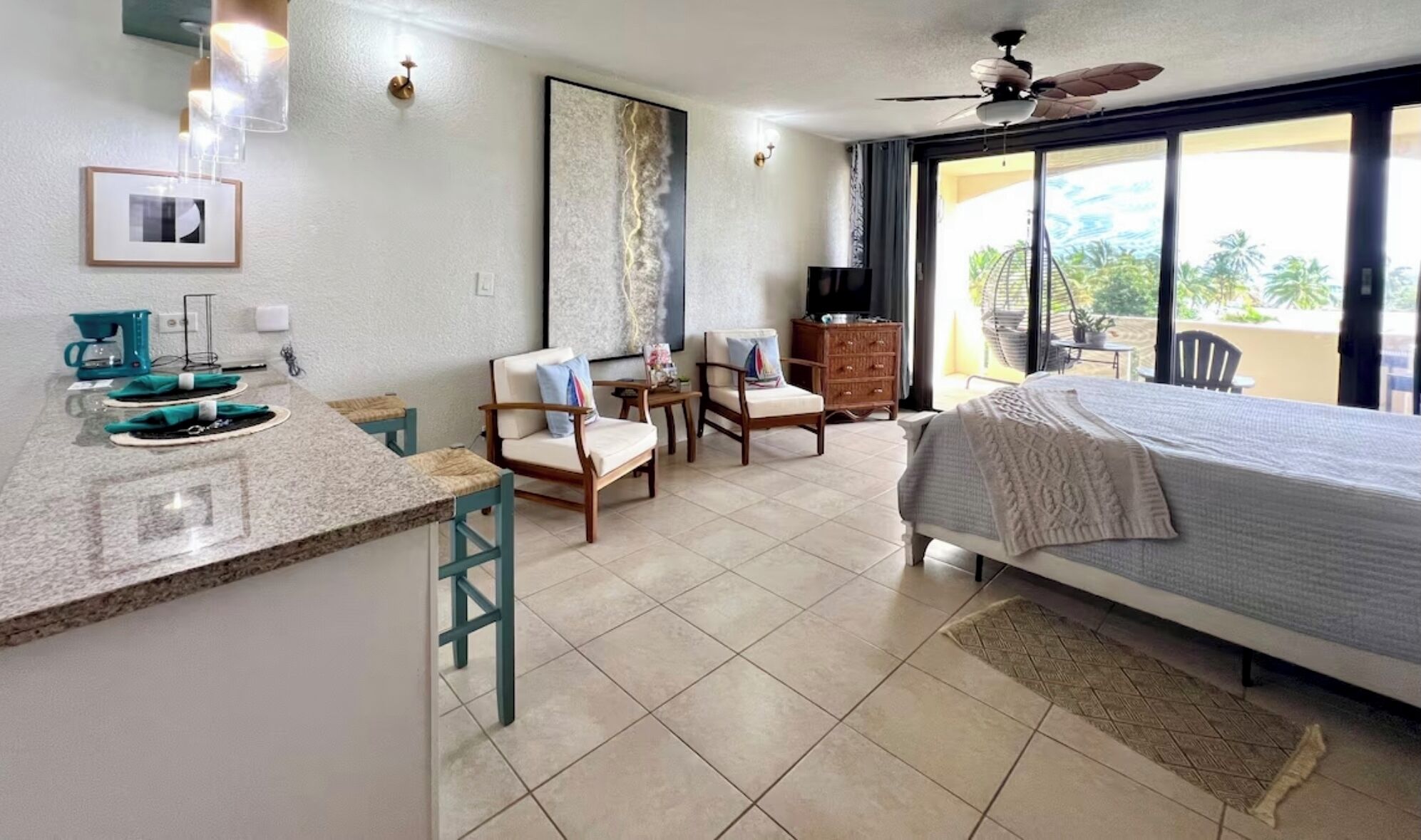 A hotel room with a bed, a desk with a coffee maker, chairs, a TV, and a balcony with a view.