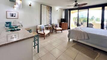 A hotel room with a bed, a desk with a coffee maker, chairs, a TV, and a balcony with a view.