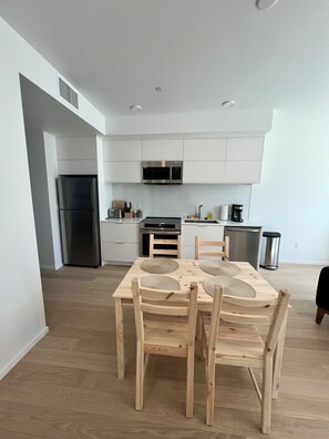 Una cocina moderna con armarios blancos, electrodomésticos de acero inoxidable y un comedor con mesa y sillas de madera.